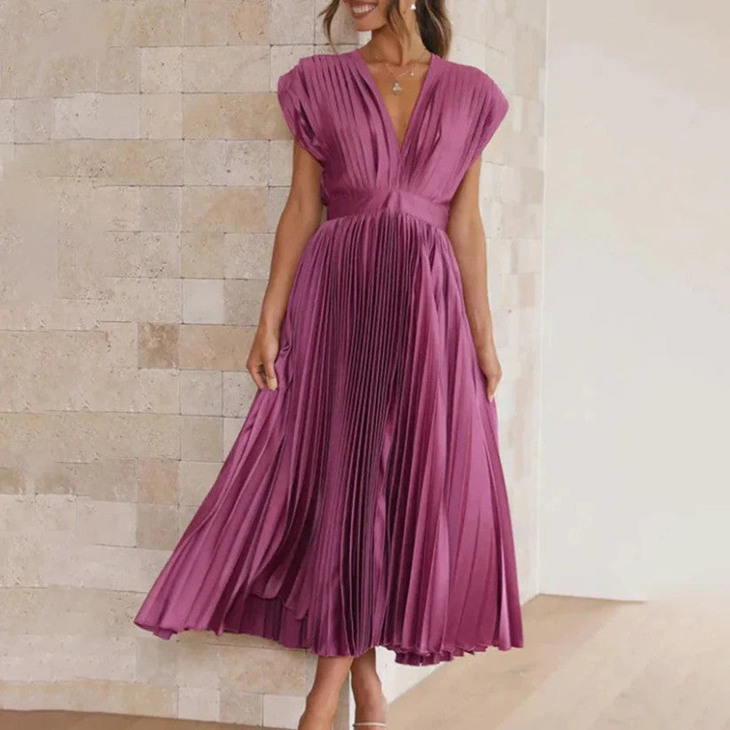 Frau in elegantem, lila Faltenkleid vor beiger Steinwand. Modisches Abendkleid, V-Ausschnitt, ärmellos, knielang. Perfekt für besondere Anlässe.