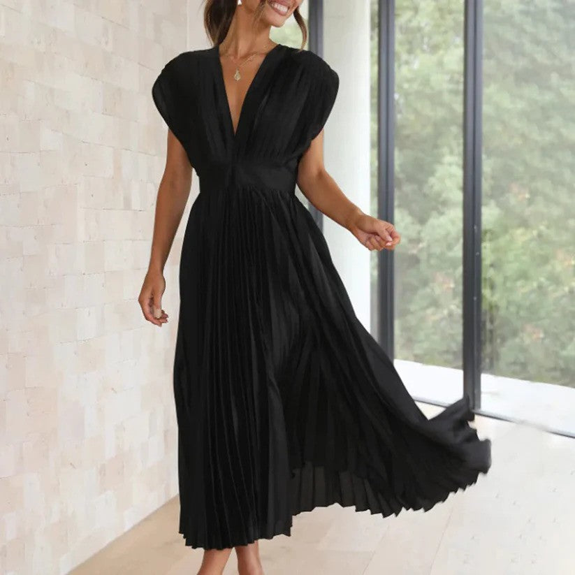 Frau in elegantem, schwarzem, plissiertem Kleid vor großen Fenstern. Stilvolle Abendmode, modernes Design, zeitloser Chic.