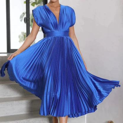 Frau in elegantem, blauem, plissiertem Kleid mit V-Ausschnitt, stehend auf Treppe. Perfekt für Abendmode, festliche Anlässe, stilvoller Look.