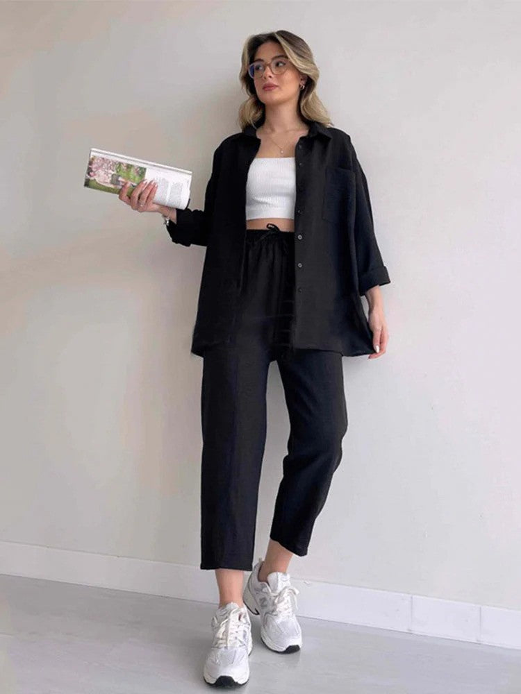 Frau in schwarzem Outfit mit weißem Top und Sneakers, hält ein Buch. Modetrend, lässiger Stil, moderne Damenmode, Streetwear-Look.
