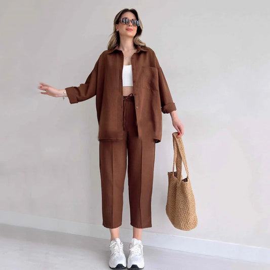 Frau in braunem Leinenanzug mit weißem Top und Sneakers, hält eine Strohtasche. Modetrend, lässiger Stil, Sommeroutfit, Damenmode.