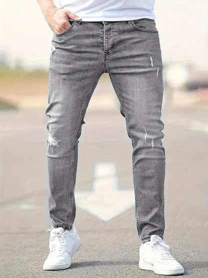 Mann in grauer, zerrissener Jeans und weißen Sneakers auf Straße. Modetrend, lässiger Stil, Herrenbekleidung, urbaner Look.