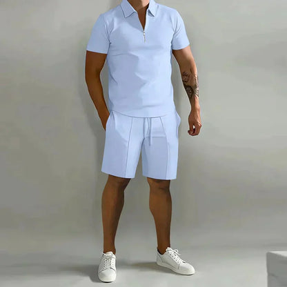 Mann in hellblauem Polo-Shorts-Set und weißen Sneakers vor grauem Hintergrund. Sommermode, Herrenbekleidung, Freizeitoutfit.