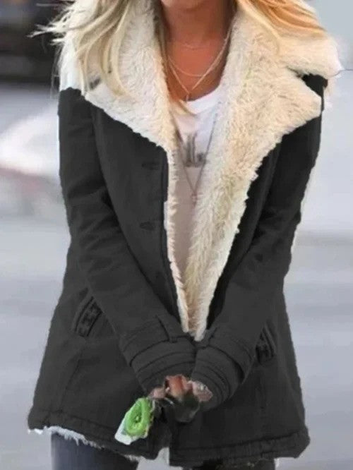 Frau in schwarzem Wintermantel mit weißem Fellkragen, hält grüne Blume. Modetrend, Winterbekleidung, stilvolle Damenjacke.