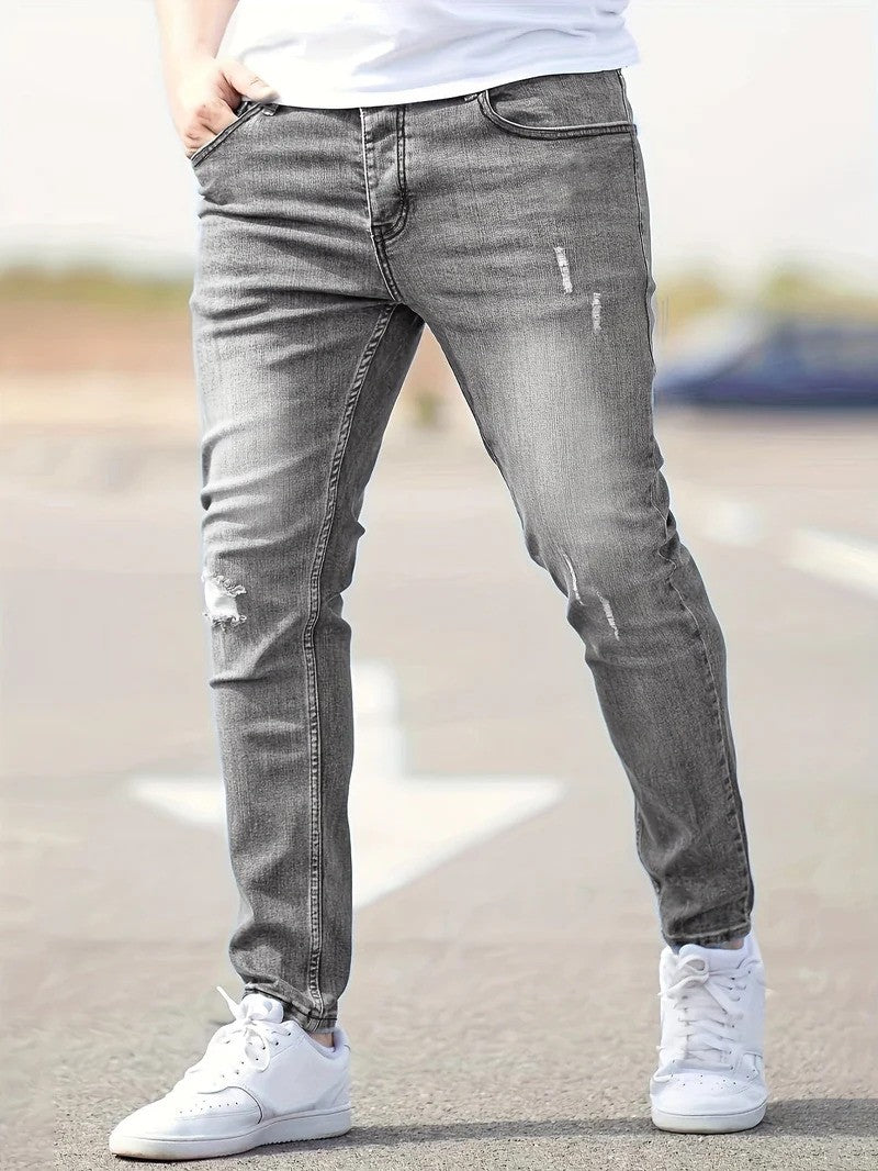 Graue Slim-Fit-Jeans für Herren, leicht zerrissen, kombiniert mit weißen Sneakers. Modischer Streetwear-Look, ideal für lässige Outfits.