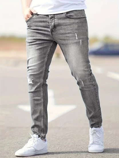 Graue Slim-Fit-Jeans für Herren, leicht zerrissen, kombiniert mit weißen Sneakers. Modischer Streetwear-Look, ideal für lässige Outfits.