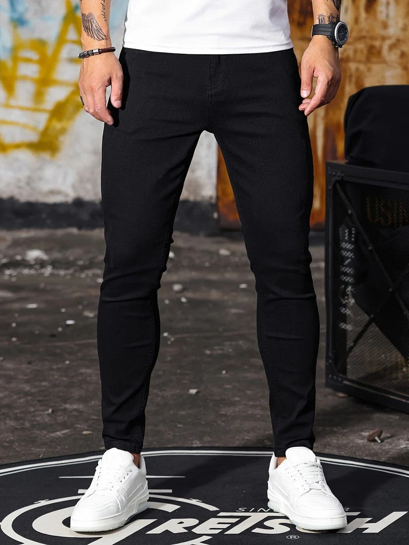 Mann trägt schwarze Skinny-Jeans und weiße Sneaker, steht auf urbanem Hintergrund. Modetrend, Herrenmode, Streetwear, lässiger Stil.