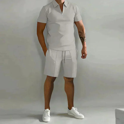 Mann in grauem Poloshirt und Shorts, weiße Sneaker, neutraler Hintergrund. Sommermode, Freizeitkleidung, Herrenoutfit, sportlich-elegant.