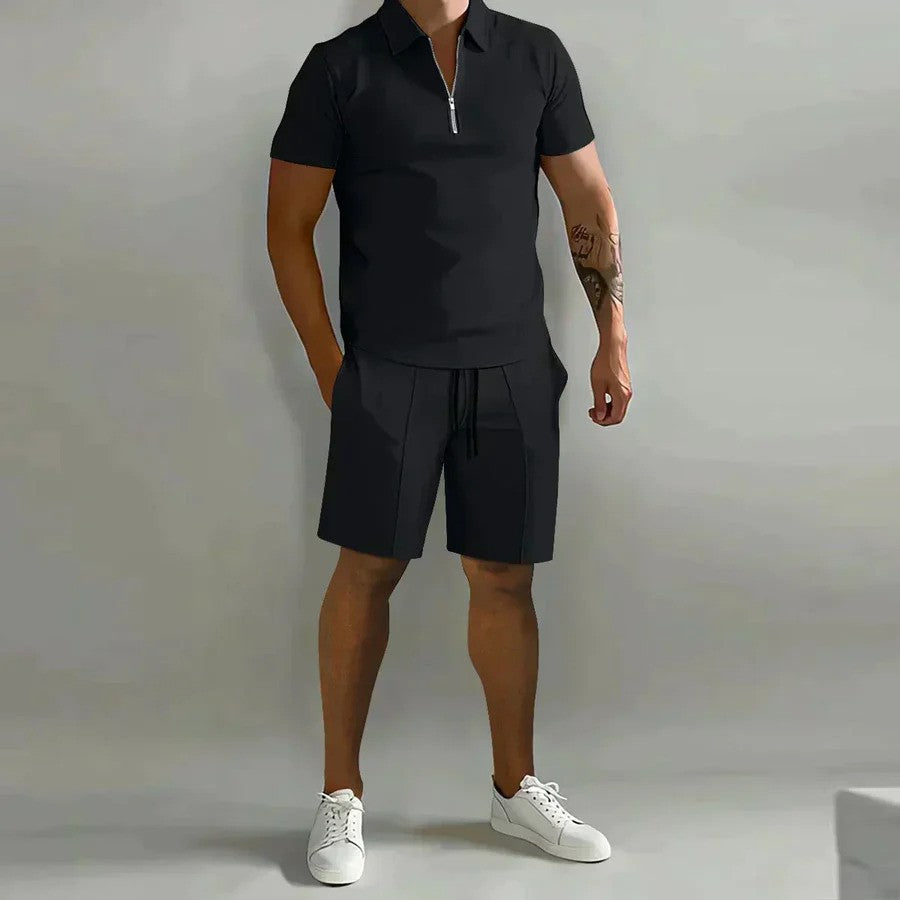 Mann in schwarzem Polohemd und Shorts, weiße Sneaker, grauer Hintergrund. Sommermode, lässiger Stil, Herrenbekleidung, sportlich-elegant.