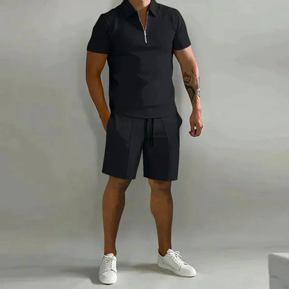 Mann in schwarzem Polohemd und Shorts, weiße Sneaker, grauer Hintergrund. Sommermode, lässiger Stil, Herrenbekleidung, sportlich-elegant.