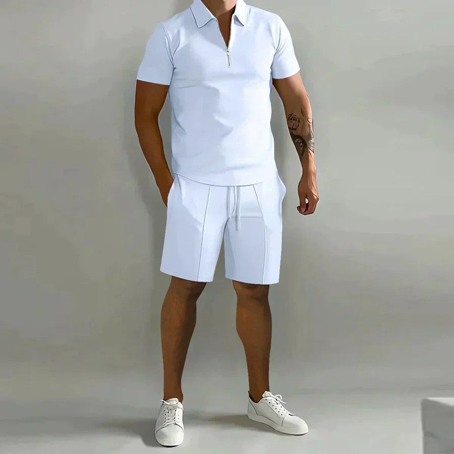 Mann in weißem Polohemd und Shorts, sportlich-eleganter Look, Sommermode, lässiger Stil, weiße Sneaker, grauer Hintergrund.