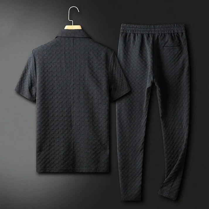 Schwarzer Herren-Trainingsanzug aus Baumwolle, bestehend aus kurzärmligem Oberteil und langer Hose, auf einem Kleiderbügel vor dunklem Hintergrund.
