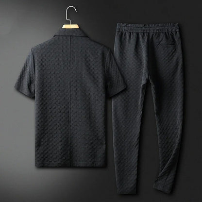 Schwarzer Herren-Trainingsanzug aus Baumwolle, bestehend aus kurzärmligem Oberteil und langer Hose, auf einem Kleiderbügel vor dunklem Hintergrund.
