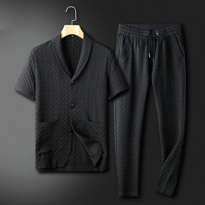 Schwarzer Herren-Pyjama-Set aus Baumwolle, bestehend aus kurzärmligem Hemd mit Knopfleiste und langen Hosen, auf einem Kleiderbügel vor dunklem Hintergrund.