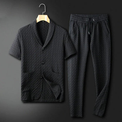 Schwarzer Herren-Pyjama-Set aus Baumwolle, bestehend aus kurzärmligem Hemd mit Knopfleiste und langen Hosen, auf einem Kleiderbügel vor dunklem Hintergrund.