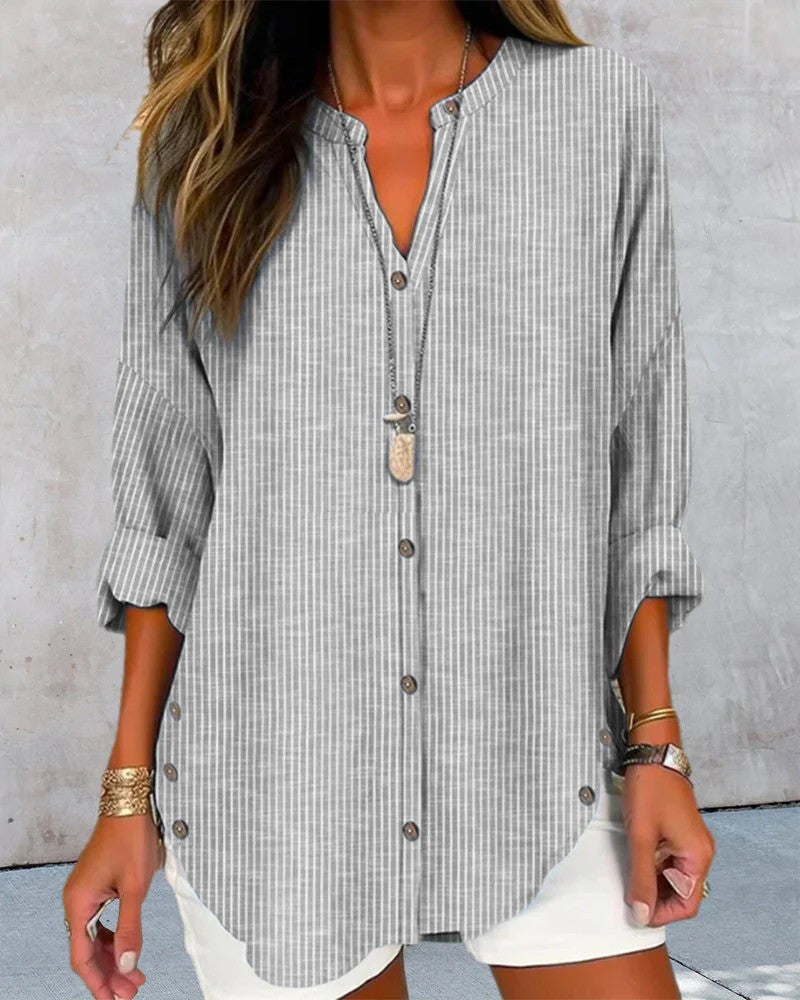 Frau in gestreifter, grauer Bluse mit Knopfleiste und weißem Rock, trägt goldene Armbänder und eine lange Halskette. Modetrend, lässiger Stil.