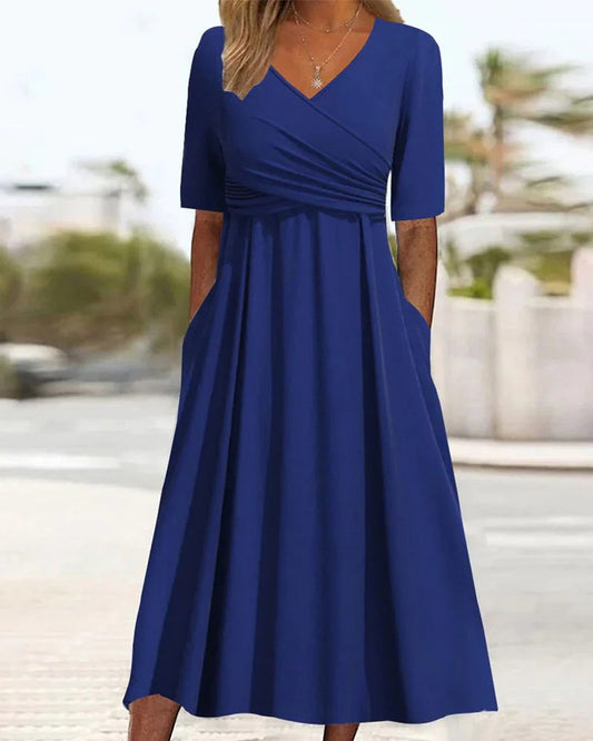 Frau in elegantem, blauem Midikleid mit V-Ausschnitt und kurzen Ärmeln, steht draußen. Perfektes Sommeroutfit, modisch und bequem.