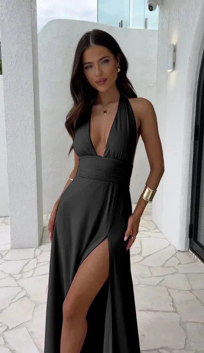 Schwarzes Abendkleid mit tiefem Ausschnitt und hohem Beinschlitz, getragen von einer Frau auf einer Terrasse. Elegantes Design, modische Abendmode.