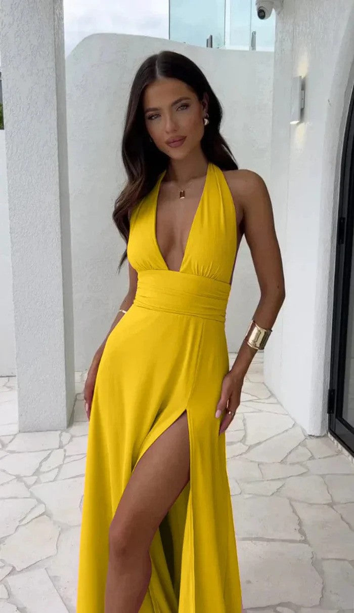Frau in gelbem Abendkleid mit tiefem Ausschnitt und hohem Beinschlitz, steht auf heller Terrasse. Elegante Mode, Sommerkleid, stilvoller Look.