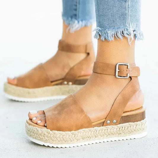 Braune Damen-Sandalen mit Keilabsatz und Knöchelriemen, kombiniert mit ausgefransten Jeans. Modische Sommerschuhe, ideal für Freizeitoutfits.