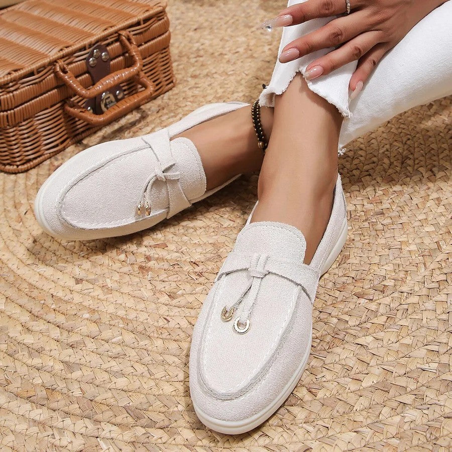 Weiße Damen-Loafer auf geflochtenem Teppich, neben einem Picknickkorb. Modische, bequeme Schuhe für Sommer und Freizeit. Elegantes Design.