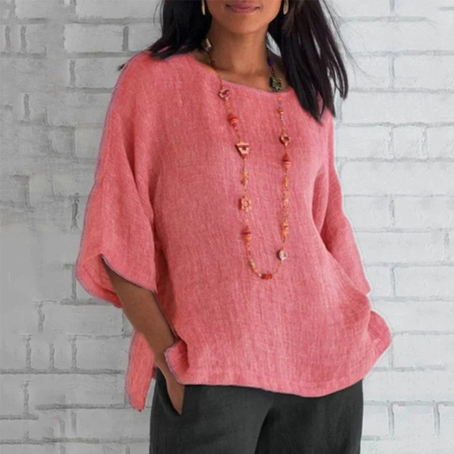 Frau in rosa Leinenbluse vor weißer Ziegelwand, trägt lange Halskette. Modetrend, lässiger Stil, Damenbekleidung, Sommeroutfit.