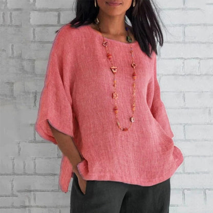 Frau in rosa Leinenbluse vor weißer Ziegelwand, trägt lange Halskette. Modetrend, lässiger Stil, Damenbekleidung, Sommeroutfit.