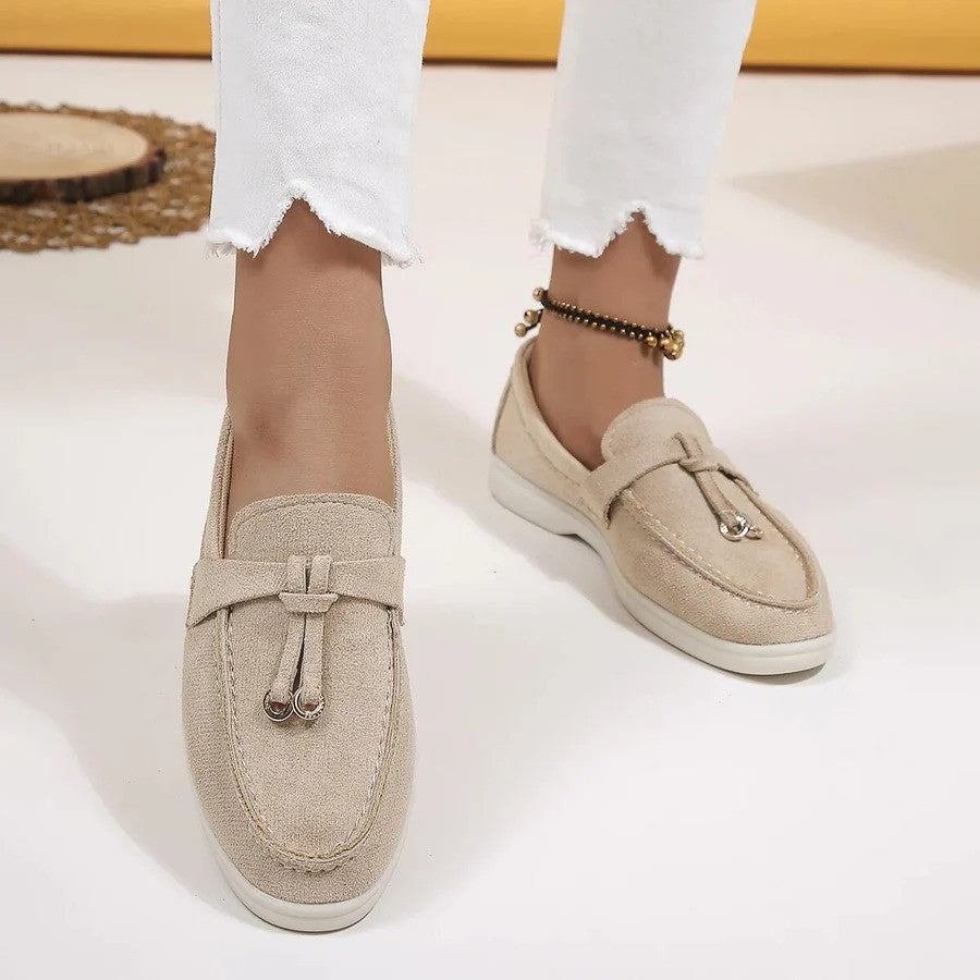 Beige Damen-Loafer aus Wildleder mit Quasten, getragen mit weißen Jeans. Modische, bequeme Schuhe für den Alltag. Ideal für Frühling und Sommer.
