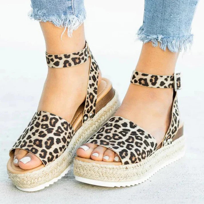 Leopardenmuster-Sandalen mit Keilabsatz und Knöchelriemen, getragen mit ausgefransten Jeans. Modische Sommerschuhe für Damen.