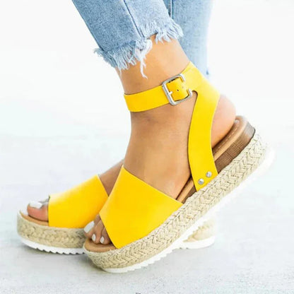 Gelbe Sandalen mit Plateau und Bastsohle, getragen von einer Person in zerrissenen Jeans. Modische Sommerschuhe, ideal für lässige Outfits.