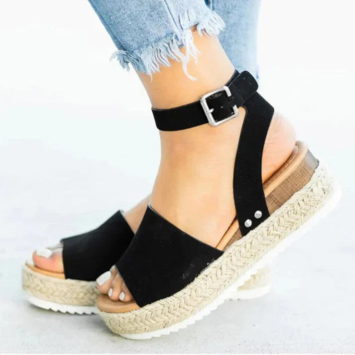 Damen Sandalen mit schwarzem Riemen, Keilabsatz aus Bast und Schnalle, getragen mit zerrissenen Jeans. Sommermode, bequeme Schuhe, trendige Sandalen.