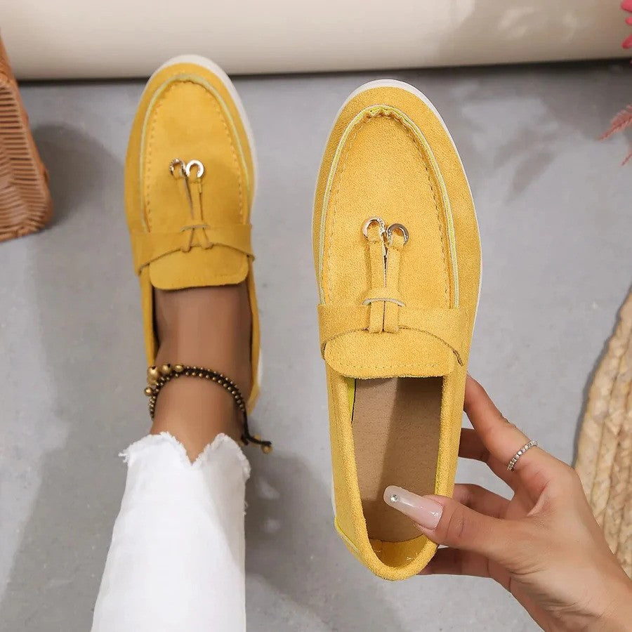 Gelbe Damen-Loafer aus Wildleder mit dekorativer Schnalle, getragen mit weißen Jeans. Modische, bequeme Schuhe für den Alltag.