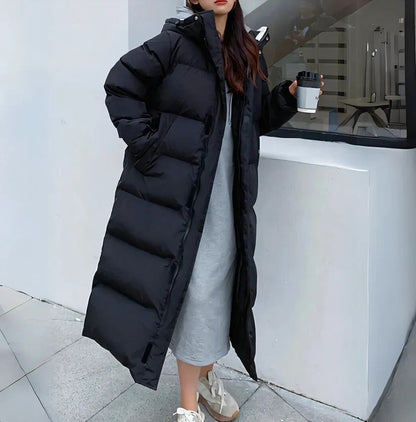 Frau in langem schwarzen Daunenmantel, hält Kaffeebecher, trägt graues Kleid und weiße Sneaker. Wintermode, Outdoor, stilvoll, warm.