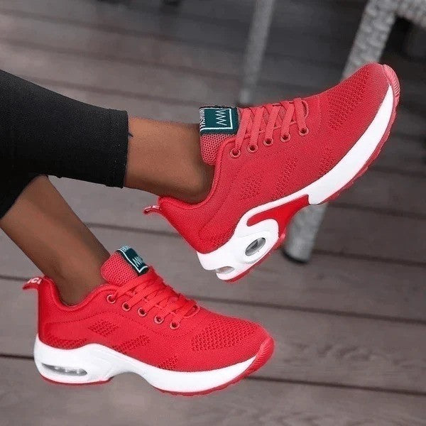 Rote Damen-Sneaker mit weißer Sohle, sportliches Design, bequem und modisch, ideal für Freizeit und Sport, auf Holzterrasse getragen.