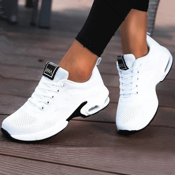 Weiße Damen-Sneaker mit Luftpolstersohle, ideal für Sport und Freizeit. Bequeme, atmungsaktive Turnschuhe auf Holzdeck.