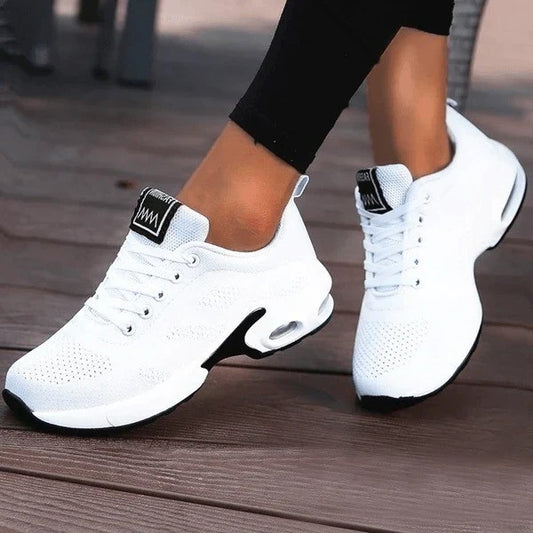 Weiße Damen-Sneaker mit Luftpolstersohle, ideal für Sport und Freizeit. Bequeme, atmungsaktive Turnschuhe auf Holzdeck.