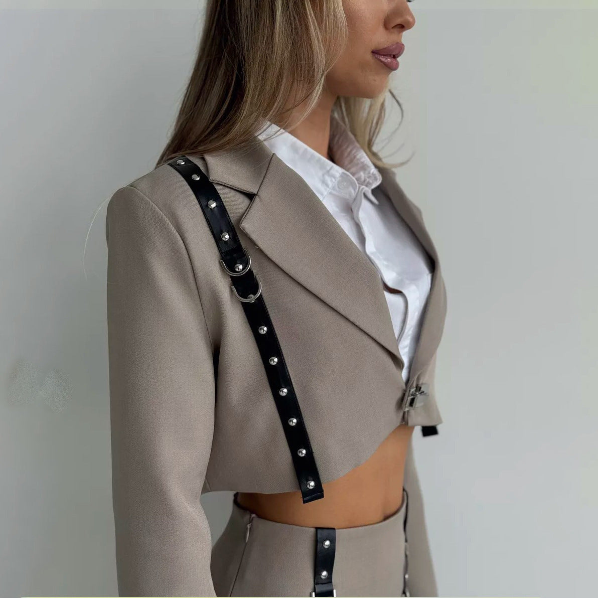 Frau in modischem, beigem Anzug mit schwarzem Riemen, weißer Bluse, modernem Design, Business-Look, elegante Damenmode, seitliche Ansicht.