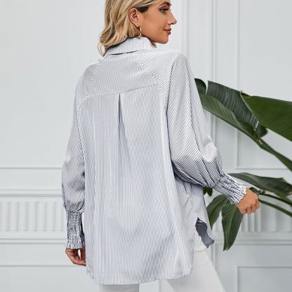 Frau in gestreifter Bluse, Rückansicht, vor weißer Wand mit grüner Pflanze. Modetrend, Damenmode, elegante Bluse, lässiger Stil.