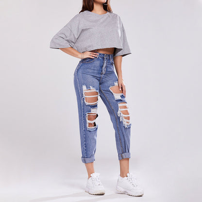 Frau in zerrissenen Jeans und grauem Crop-Top, trägt weiße Sneaker. Modetrend, lässiger Streetstyle, moderne Damenbekleidung.