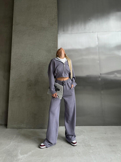 Frau in grauem Jogginganzug posiert vor grauer Wand, trägt weiße Sneakers. Modetrend, lässiger Stil, urbane Kleidung, Streetwear.