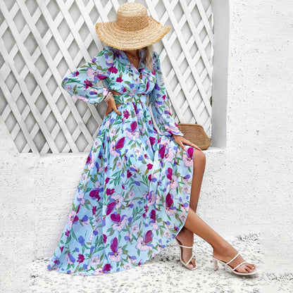 Frau in langem, geblümtem Kleid und Strohhut sitzt vor weißer Wand. Sommermode, elegantes Blumenkleid, stilvolle Accessoires, Freizeitlook.