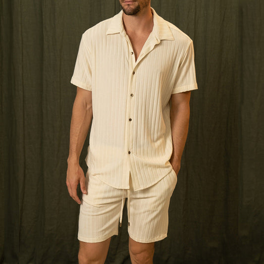 Mann trägt cremefarbenes, gestreiftes Kurzarmhemd und Shorts vor dunklem Hintergrund. Sommermode, Herrenbekleidung, Freizeitlook.