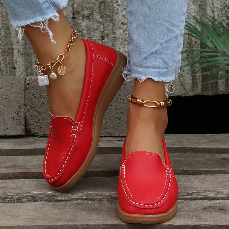 Rote Damen-Loafer aus Leder mit weißer Naht, getragen mit hellblauen Jeans und goldenen Fußkettchen. Modische Schuhe für Damen.