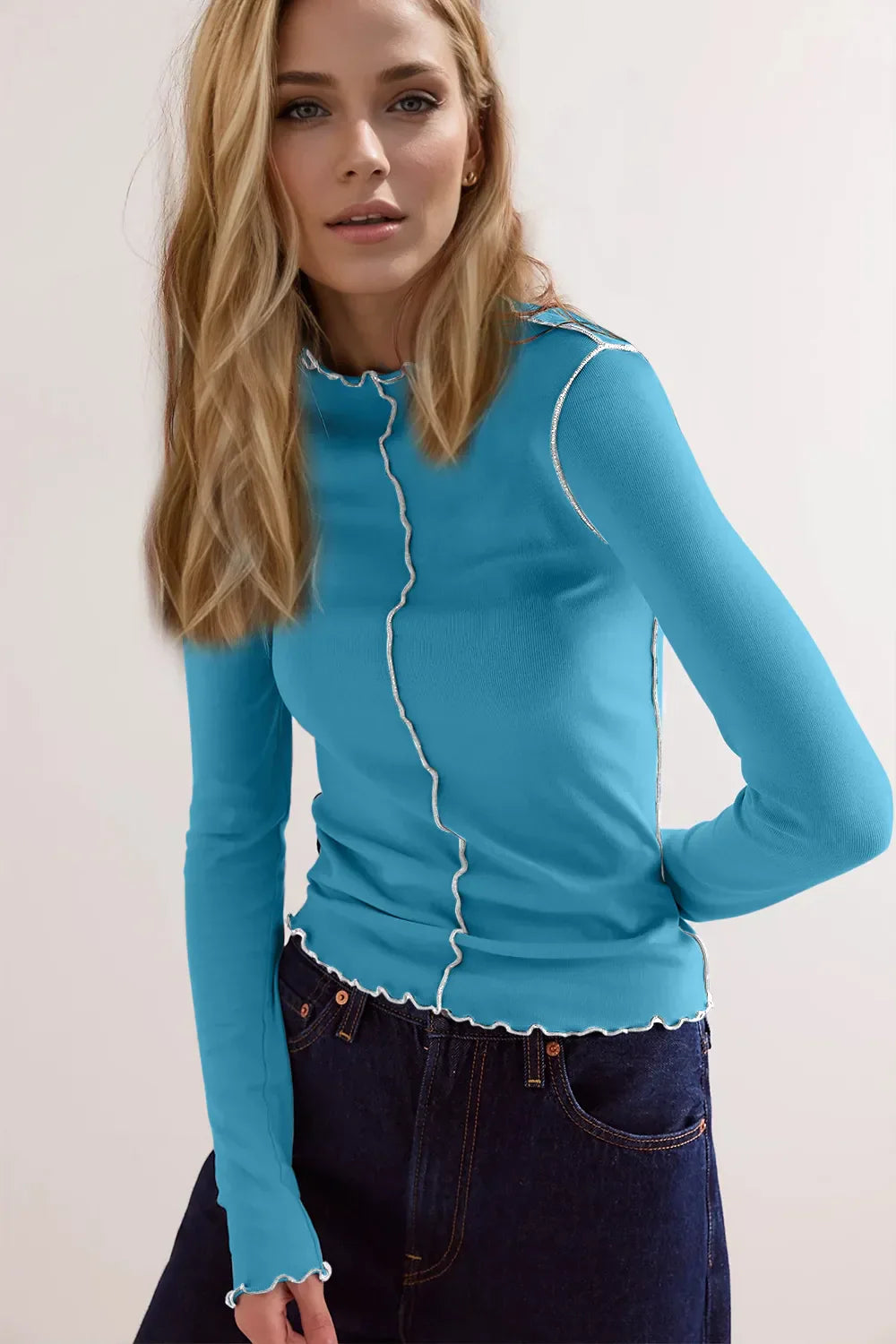 Blonde Frau in blauem Langarmshirt mit weißen Nähten und dunkler Jeans. Modetrend, Damenbekleidung, Freizeitlook, stilvolles Outfit.