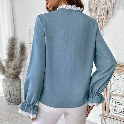 Frau in hellblauer Bluse mit Spitzenkragen und Rüschenärmeln, steht in modernem, hell eingerichtetem Raum. Elegante Damenmode, stilvoller Look.