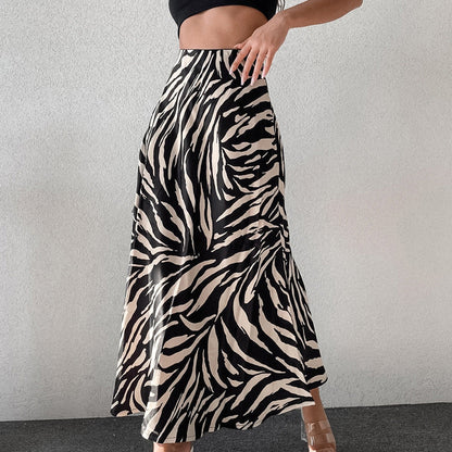 Frau in schwarz-weißem Zebra-Muster Maxirock, modisch, trendig, Sommermode, eleganter Look, stehend vor grauer Wand.