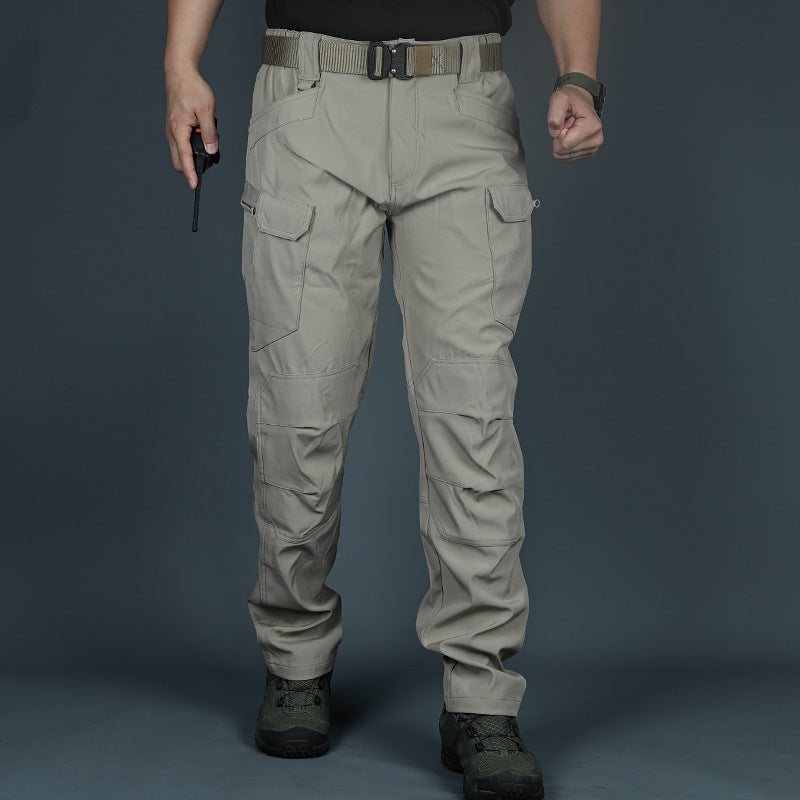 Mann in taktischer Hose, beige, mit Taschen und Gürtel, hält Funkgerät. Outdoor-Kleidung, robust, ideal für Wandern und Abenteuer.