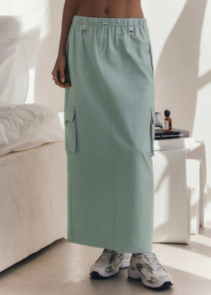 Damen in mintgrünem Cargo-Rock mit Taschen, kombiniert mit weißen Sneakern. Moderner Streetstyle, ideal für lässige Sommermode.