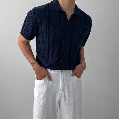 Mann in dunkelblauem Strickpolo und weißen Hosen, Hände in den Taschen. Stilvolle Herrenmode, lässiger Look, Sommeroutfit.