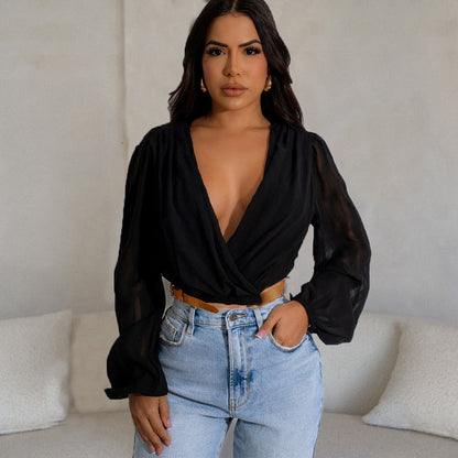 Frau in schwarzer Bluse mit tiefem Ausschnitt und blauer Jeans posiert vor beigem Hintergrund. Modetrend, Damenmode, stilvolle Kleidung.